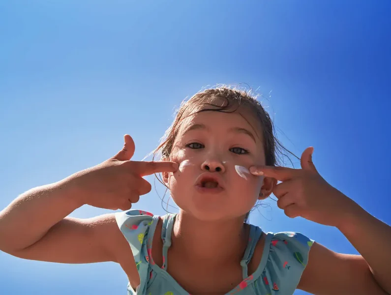 Criança a colocar protetor solar infantil na cara.