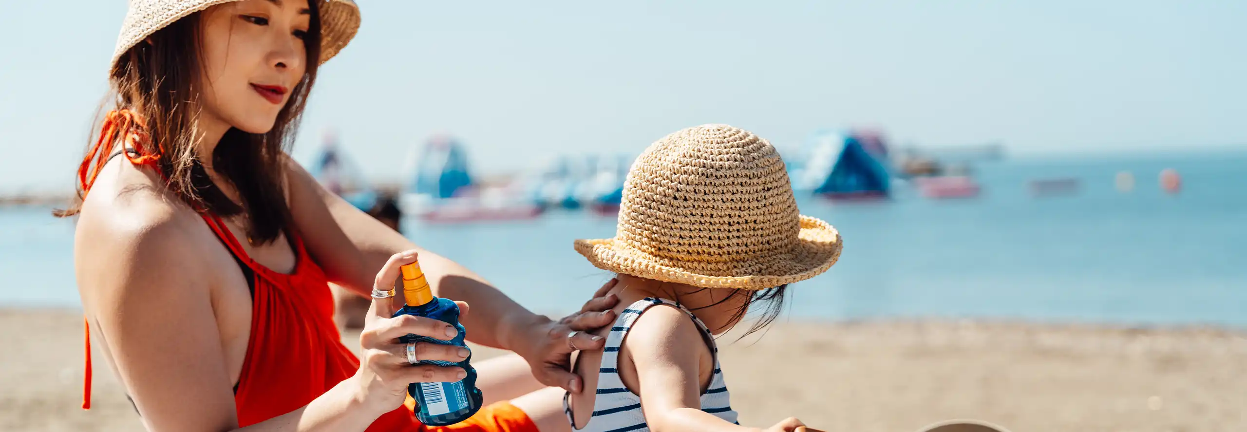mãe e criança a colocar protetor solar infantil na praia.