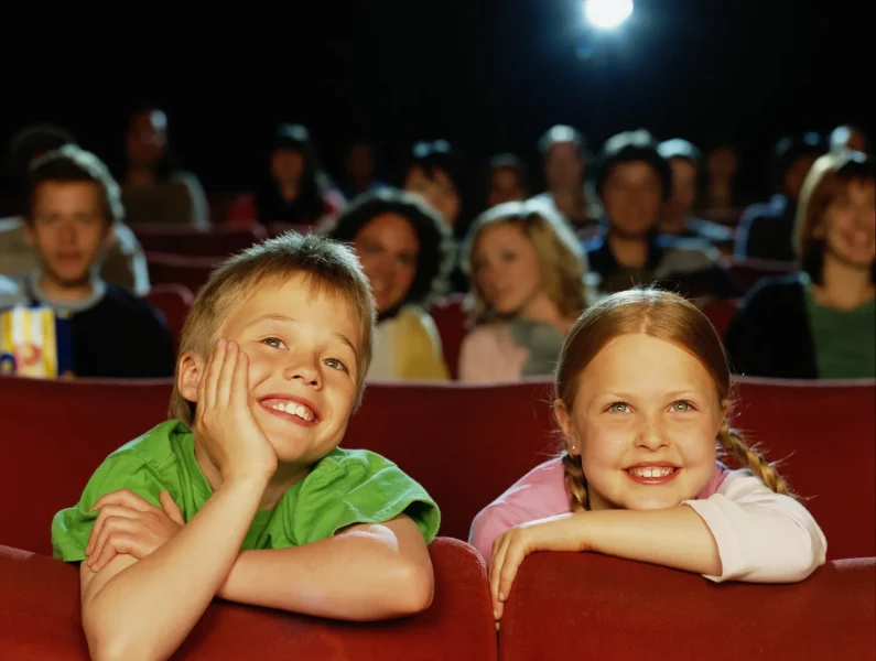 menino e menina sentados no cinema/teatro a sorrirem para o palco
