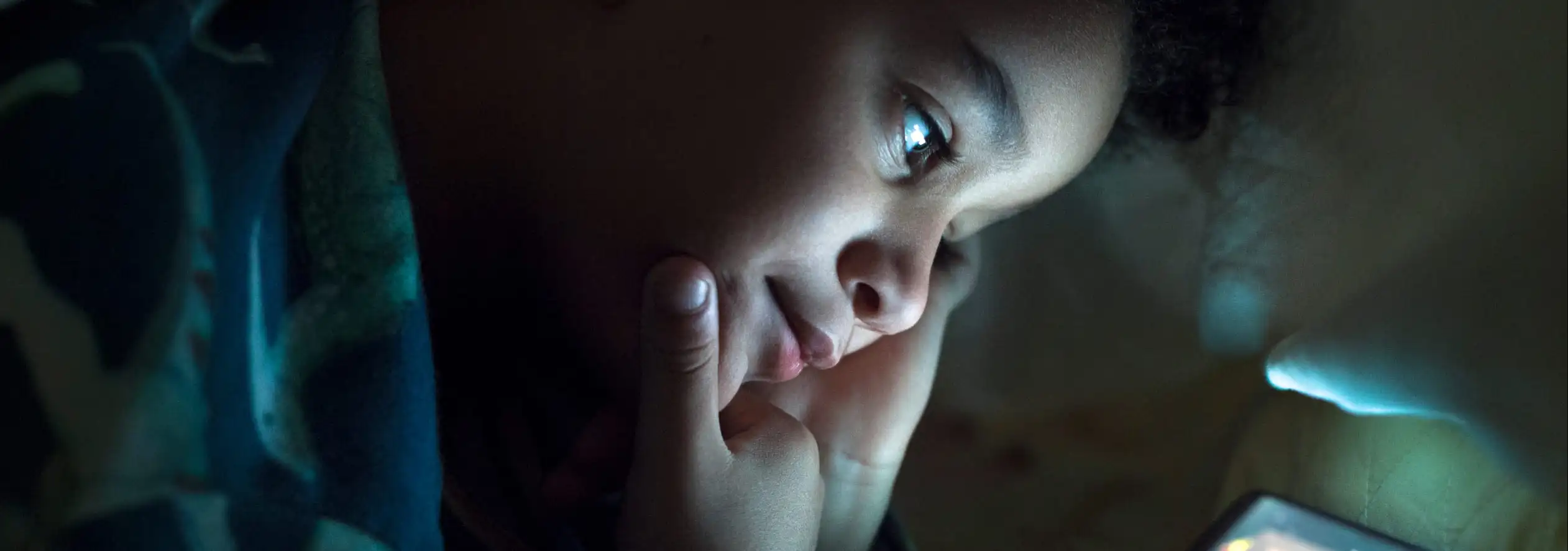 Rapaz a jogar videojogo à noite escondido dos pais, ilustrando a necessidade de uma aplicação de controlo parental.