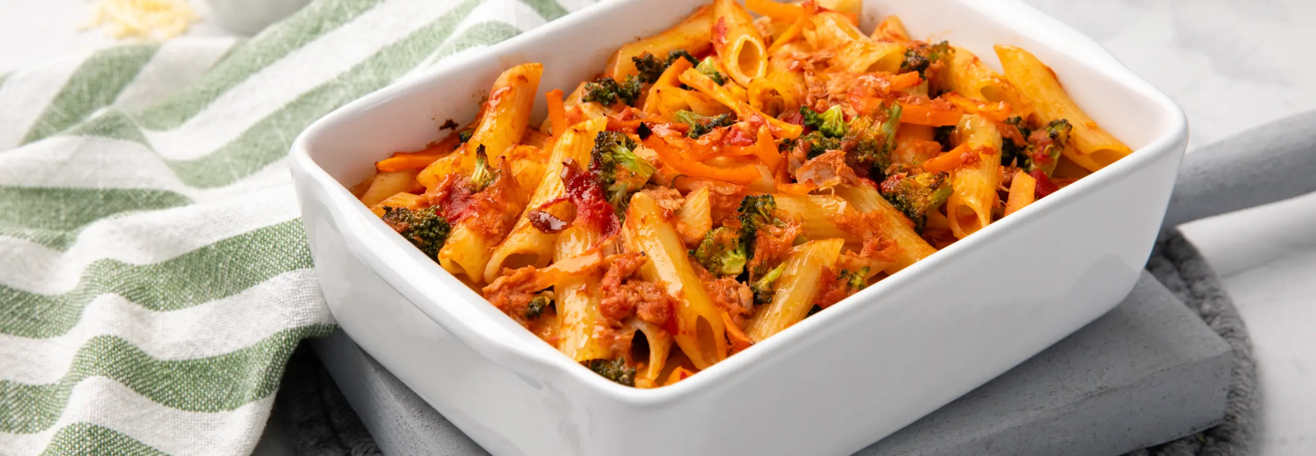 Massa no forno com atum e legumes servida numa travessa, com vegetais visíveis e crosta dourada.