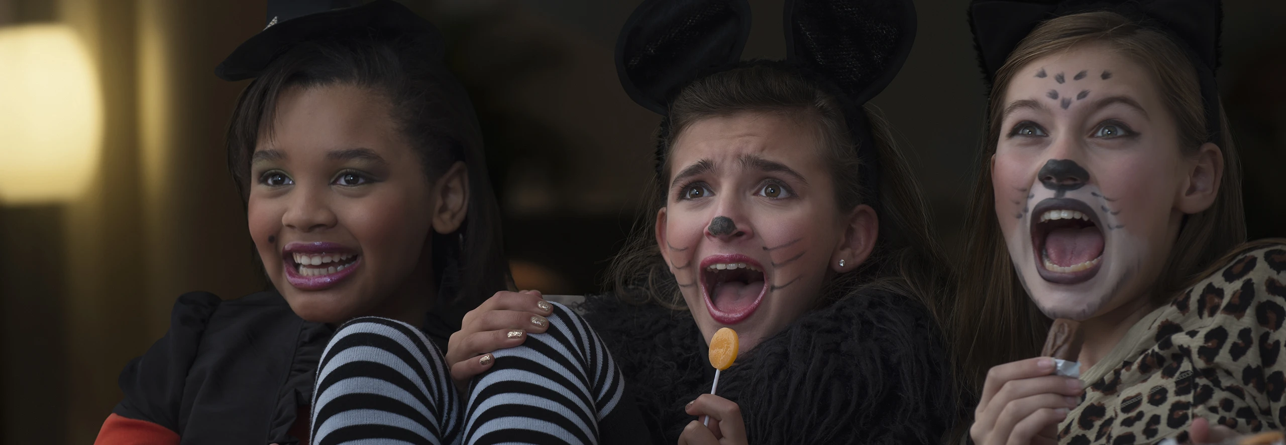 Crianças em fantasia de Halloween sentadas juntas a ver um filme assustador, partilhando expressões divertidas de surpresa.