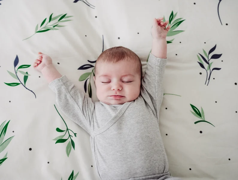 Bebé esticando os braços enquanto está deitada na cama, num momento de despertar suave e acolhedor.