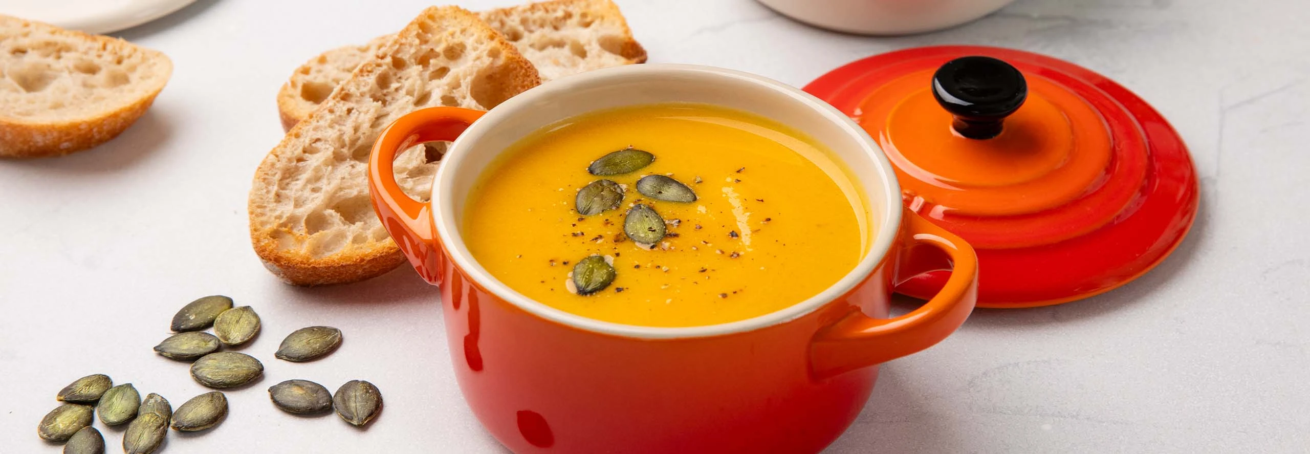 Taça de creme de abóbora decorada com um fio de natas, apresentada sobre fundo escuro