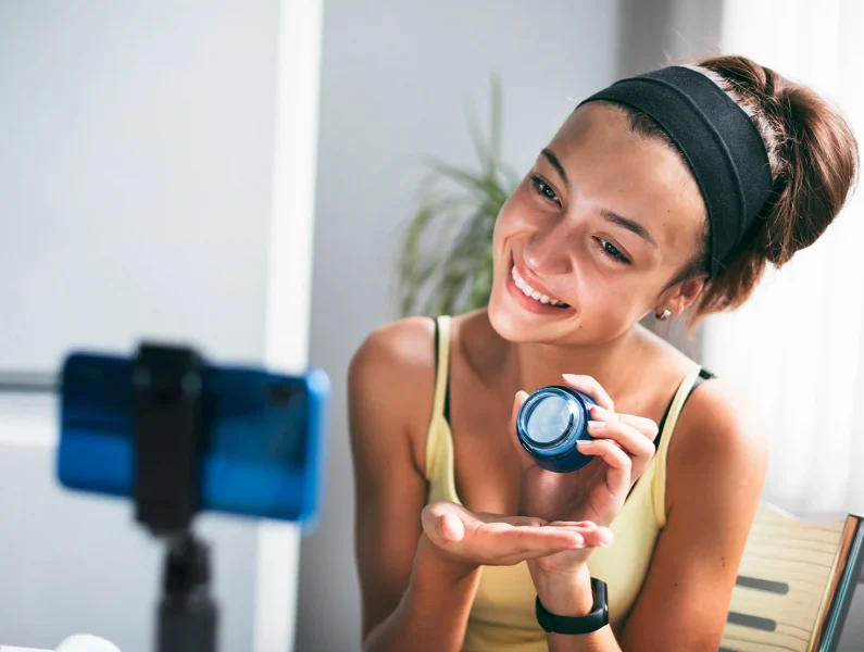 Adolescente feliz a gravar conteúdo de cuidado da pele com o smartphone, mostrando como as redes sociais influenciam a expressão e a criatividade das crianças.