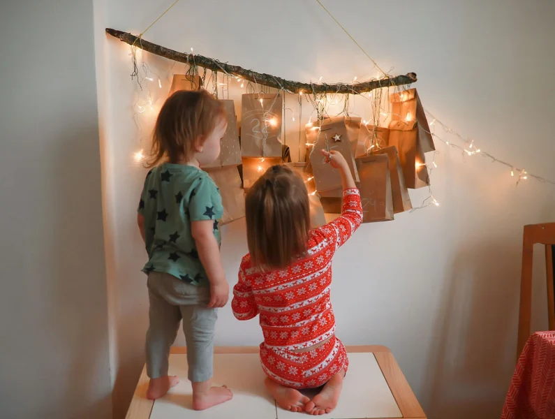 Crianças a abrir um calendário de advento pendurado numa parede.
