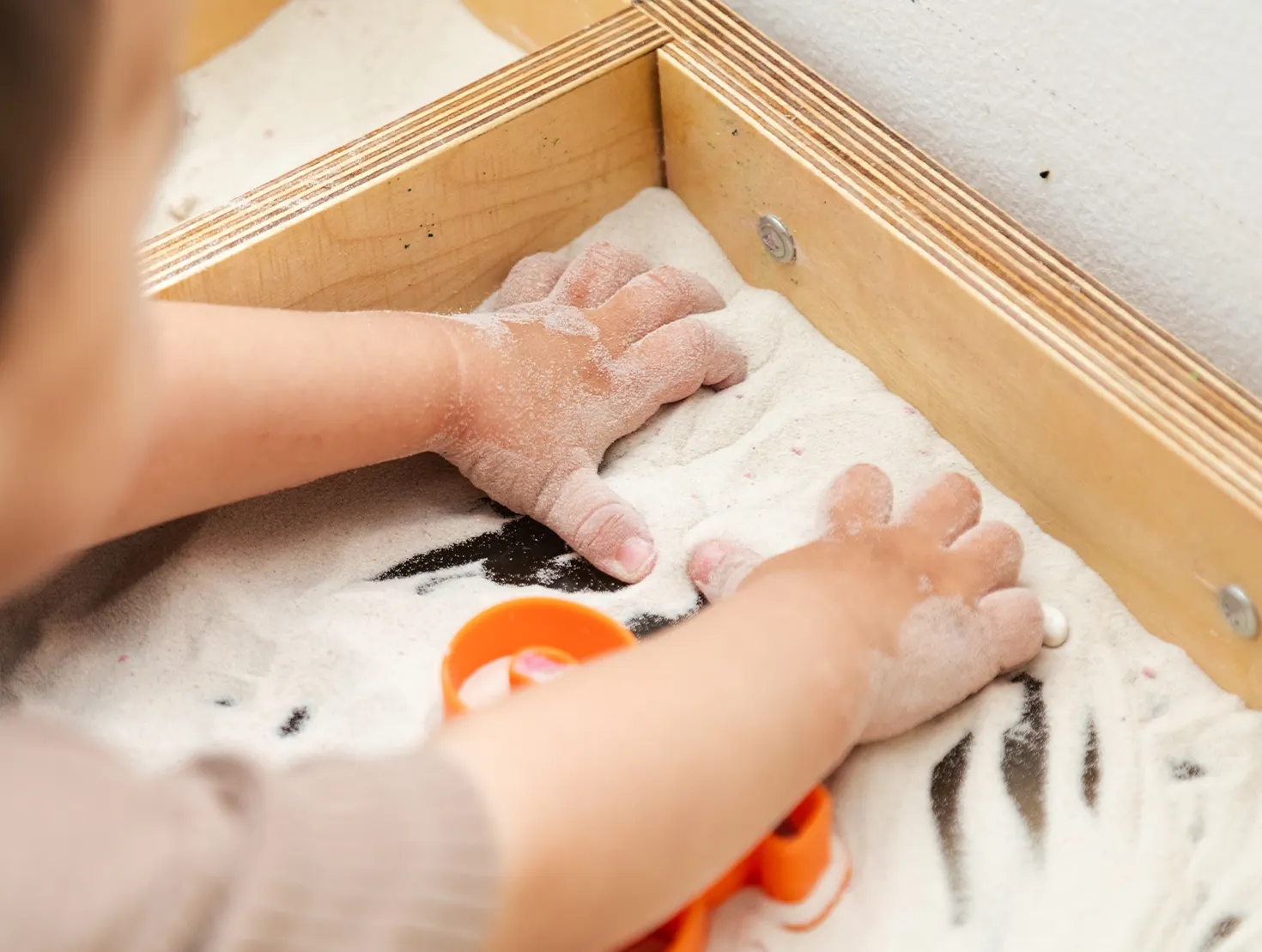 Criança a explorar diferentes texturas numa caixa de areia.
