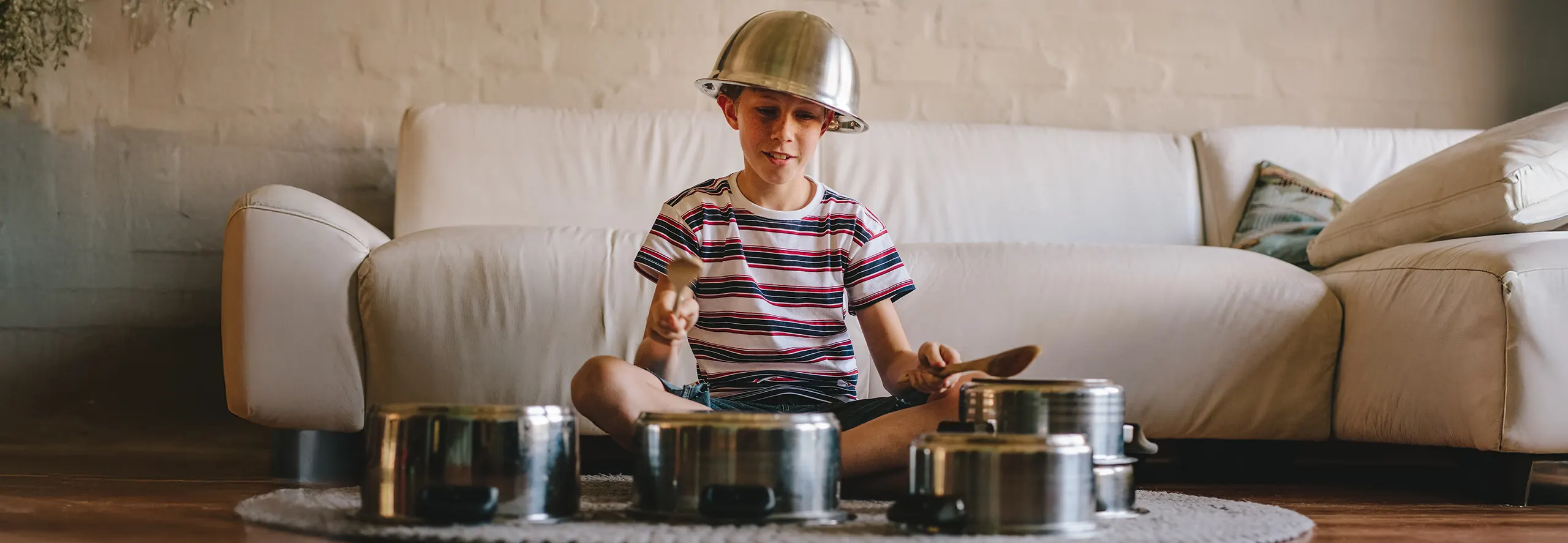 Criança sentada no chão a tocar música com panelas e utensílios de cozinha.