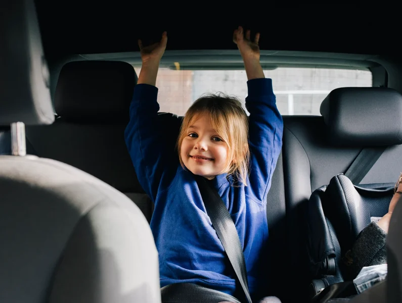 Criança sentada no banco traseiro do carro, com cinto de segurança bem posicionado e postura adequada.
