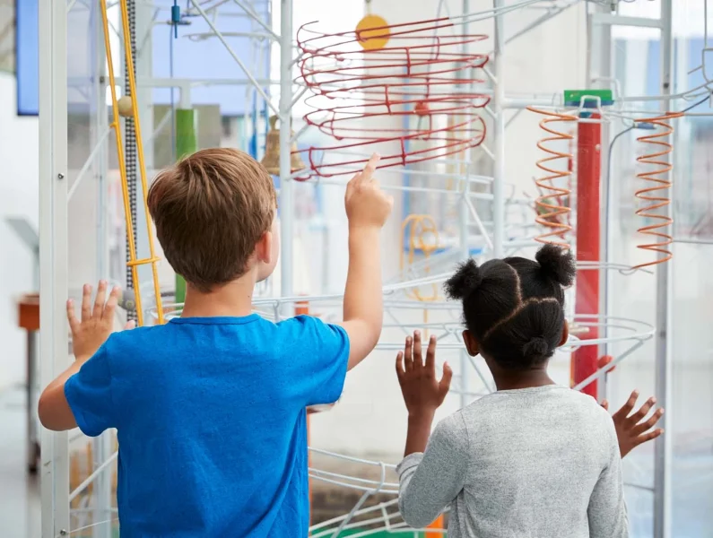 Crianças a explorar uma instalação científica interativa num museu durante uma atividade educativa de verão.